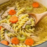 Gordon Ramsay Chicken Noodle Soup with noodles, carrots, and herbs in a pot