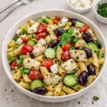 A colorful bowl of Mediterranean Chicken Pasta Salad on a wooden table.