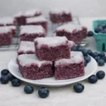 A stack of Glazed Blueberry Brownies with white sugar glaze and fresh berries.