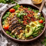 A vibrant bowl of Grilled Lemon Herb Chicken Avocado Orzo Salad topped with grilled chicken.