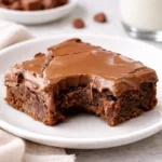 A stack of Lunch Lady Brownies with thick chocolate frosting on a wooden board.