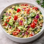 A vibrant bowl of Mediterranean Orzo Pasta Salad on a wooden table.