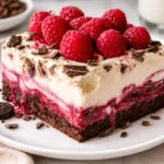 A layered Raspberry Chocolate Lasagna Dessert in a glass dish with fresh raspberries on top.
