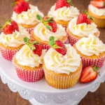 A moist Tres Leches Cupcake with white frosting and a fresh strawberry on top.